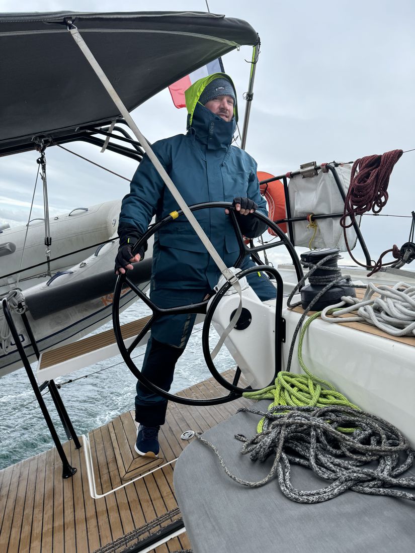 Michael Renfer in sailing gear, steering a sailboat at the wheel